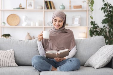 En sevdiği eğlence yeri. Rahat Müslüman kız kitap okuyor ve evde çay içiyor.