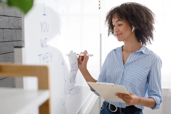 Trabajo remotamente tutor. Mujer amigable con auriculares escribe con marcador en pizarra — Foto de Stock