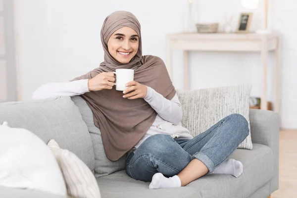 Waktunya minum teh. Smiling Muslim Woman Relaxing On Couch With Hot Drink — Stok Foto