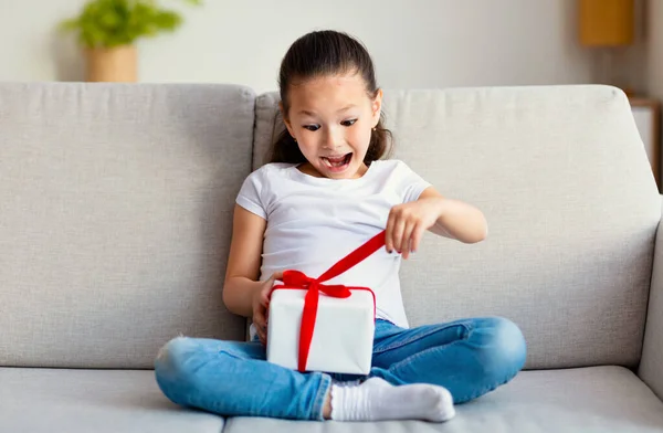 Excited Asian Little Girl Opening Gift Box Sitting At Home — Stock Photo, Image