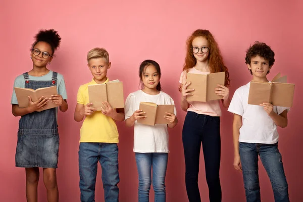 Grupo de escolares adorables con libros de texto posando sobre fondo de estudio rosa —  Fotos de Stock