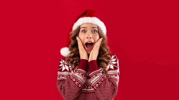 Celebración de Navidad. Mujer joven emocionada en sombrero de Santa y suéter de invierno caliente sobre fondo rojo — Foto de Stock