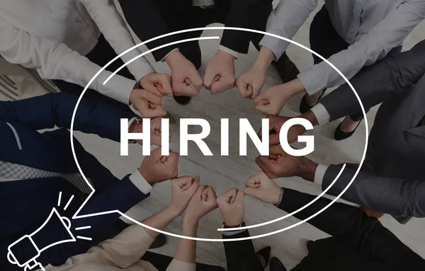 Young business people putting their fists together as symbol of unity, top view. Collage with word HIRING in speech bubble — Stock Photo, Image