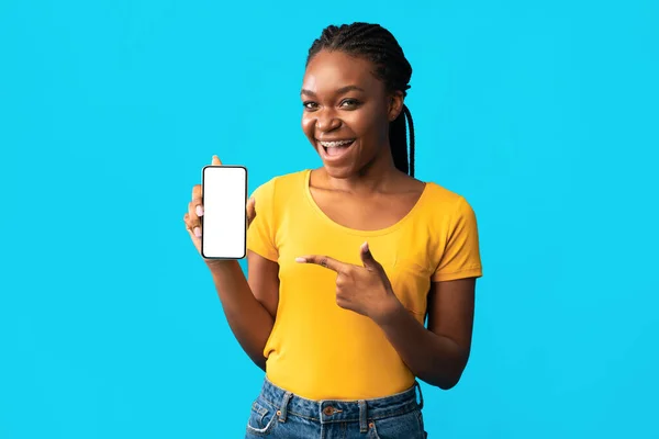 Африканська дівчина показує мобільний телефон порожній екран на синьому фоні — стокове фото