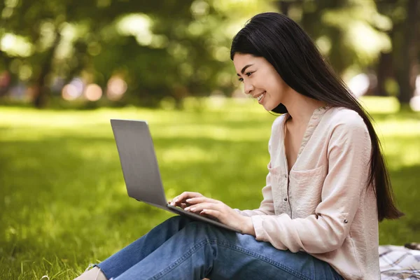 Feliz joven asiática chica freelancer trabajando en ordenador portátil en parque —  Fotos de Stock