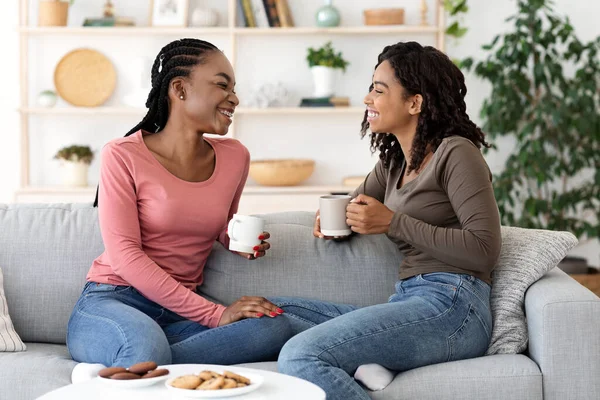 Fekete barátnők élvezik a hétvégét együtt, kávét isznak a kanapén — Stock Fotó