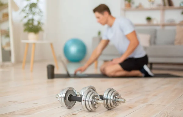 Dumbbells close up, young man sitting on mat and working on laptop with sport equipment — Stock Photo, Image