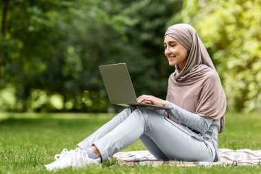 Güzel müslüman kız parkta dinlenirken dizüstü bilgisayar kullanıyor.