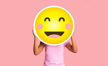 Siyah kız pembe arka planda mutlu utangaç emojinin arkasına saklanıyor.