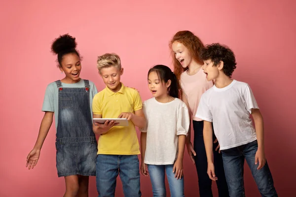 Izgalmas iskolás fiúk és iskolás lányok nézi tabletta számítógép rózsaszín háttér — Stock Fotó