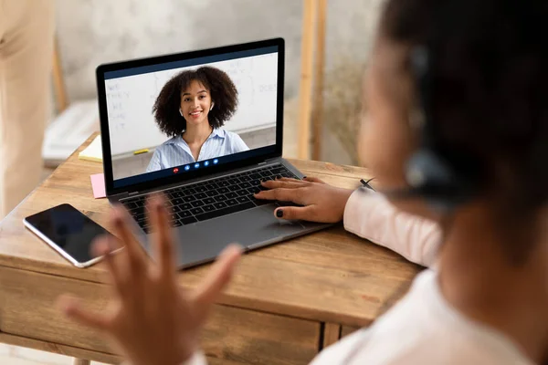 Studentessa nera al computer portatile saluto insegnante sullo schermo del computer al coperto — Foto Stock