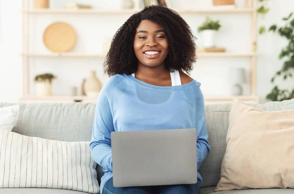 Černá žena sedí na gauči s PC při pohledu na kameru — Stock fotografie