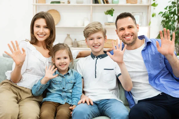 Família de quatro acenando Olá cumprimentando sentado no sofá interior — Fotografia de Stock