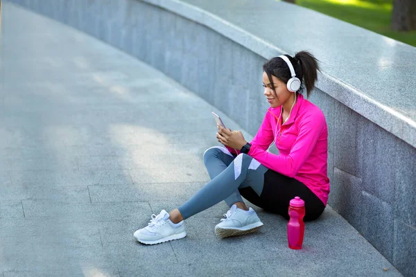 Menina negra ouvindo música, descansando enquanto jogging no parque — Fotografia de Stock