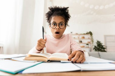 Ev ödevi yaparken, evde kitap başında otururken şok olmuş zenci kız pozu.