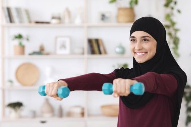 Türbanlı spor kızı evde dambıllarla eğitim görüyor.