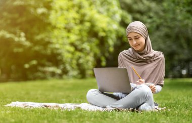 Arap kadın, parkta dizüstü bilgisayarla çalışıyor.