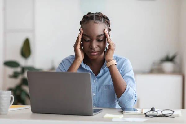 Перегруженная работой чернокожая деловая женщина, страдающая головной болью в офисе, массирующая виски — стоковое фото