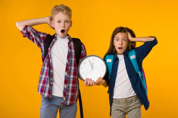 Zaskoczony mały chłopiec i dziewczynka trzymając zegar w studio — Zdjęcie stockowe