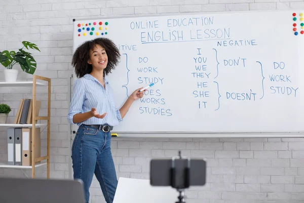 Online lesson for students. Smiling girl points at blackboard and teaches english at webcam