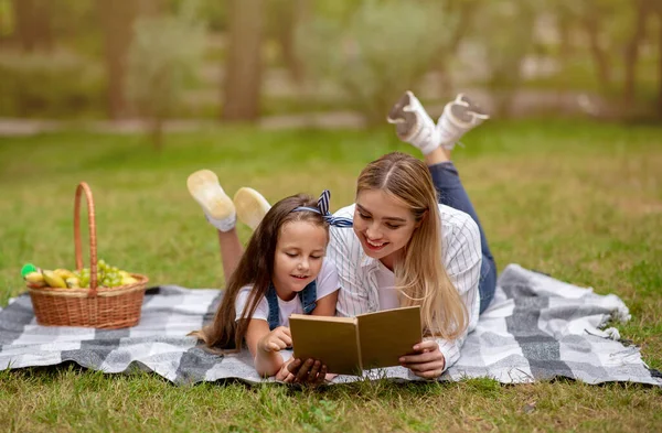 Söt mamma och dotter ligger på rutig läsa bok utanför — Stockfoto