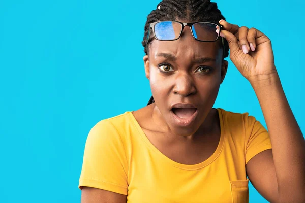 Discontented Black Girl Looking At Camera Rising Eyeglasses, Blue Background — Stock Photo, Image