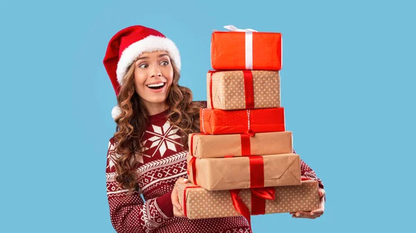 Chica bonita en sombrero de Santa y suéter de punto con un montón de regalos de Navidad sobre fondo azul — Foto de Stock