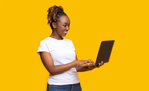 Happy african girl typing on laptop, chatting with friends