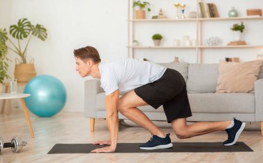 Spor, esneme, evde online egzersiz. Oturma odasının iç tarafındaki eğitimli adama odaklanmış.