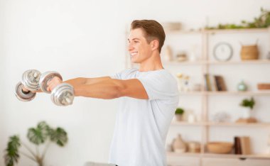 Evdeki spor blogu için basit egzersizler ve video çekimi. Gülümseyen adam dambıllarla egzersiz yapıyor.