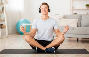 Evde müzikle modern egzersiz. Kulaklıklı gülen adam yoga ve meditasyondan hoşlanıyor.
