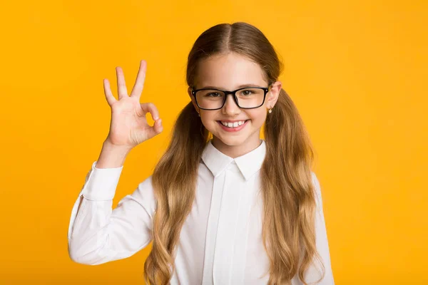 Alegre escola menina gestos OK posando no amarelo estúdio fundo — Fotografia de Stock