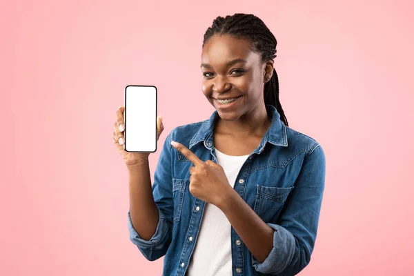 Afro-Amerikaanse vrouw toont mobiele telefoon blanco scherm over roze achtergrond — Stockfoto