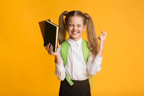 Estudante mantendo os dedos cruzados antes do teste da escola em pé, fundo amarelo — Fotografia de Stock