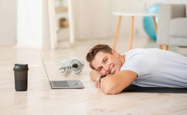 Çevrimiçi egzersiz ve dinlenme. Oturma odasında dizüstü bilgisayarla yerde yatan gülümseyen adam. — Stok fotoğraf