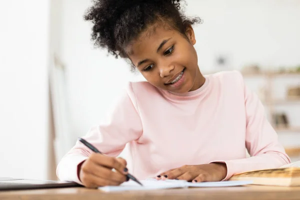 Africana adolescente chica haciendo tarea escritura en ejercicio-libro en casa —  Fotos de Stock