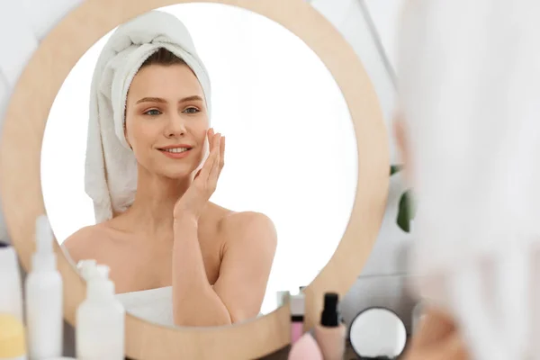 Cheerful young woman applying beauty product on her face — Stock Photo, Image