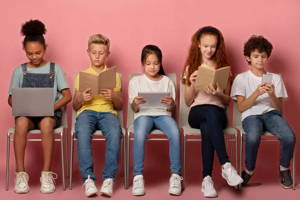 Concept d'apprentissage en ligne. Focalisé divers écoliers avec des gadgets et du matériel d'étude assis sur des chaises sur fond rose — Photo