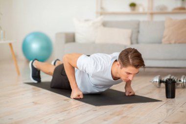 Evde yalnızım ve salgın sırasında antrenman yapıyorum. Sporcu spor malzemeleriyle paspasın üzerinde şınav çeker.