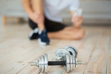 Spor giyimli ve spor ayakkabılı bir adam, yerde oturuyor ve halterli akıllı telefonların başında oturuyor.