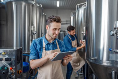 Bira fabrikasında kalite kontrol. Çocuklar çaydanlığın yanında tablet kullanarak çalışırlar.