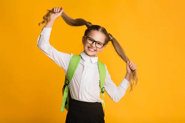 Pequena estudante brincando com o cabelo posando no fundo amarelo — Fotografia de Stock