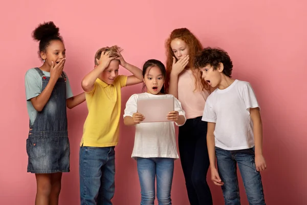 Gruppe überraschter multiethnischer Freunde, die gemeinsam etwas auf einem Tablet-Computer anschauen, rosa Hintergrund — Stockfoto