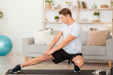 Sabahları covid-19 sırasında esneme ve egzersiz. Spor giyim işindeki kaslı adam evde çalışıyor.