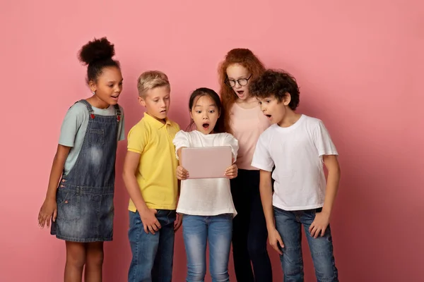 Geschokte kinderen staren samen in tablet scherm, verbaasd over iets, roze achtergrond — Stockfoto