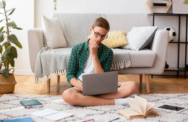 Scolaretto intelligente che fa i compiti, usa il computer portatile, legge libri — Foto Stock