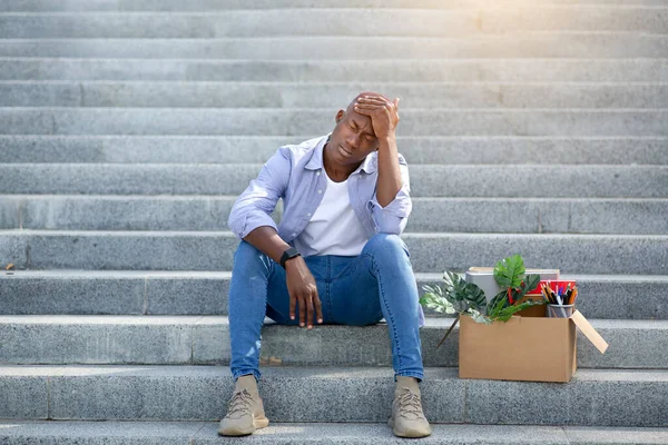 Tipo negro deprimido con pertenencias personales sentado en las escaleras después de perder su trabajo, al aire libre — Foto de Stock