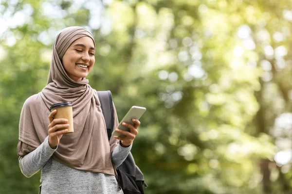 Müslüman kız tesettürlü kahve içiyor ve telefon kullanıyor. — Stok fotoğraf
