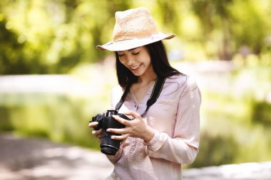En sevdiği hobi. Neşeli Asyalı Kadın Profesyonel Kamerayla Açık havada Fotoğraf Çekiyor
