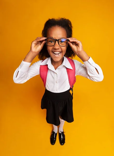 Colegiala africana mirando a la cámara a través de anteojos sobre fondo amarillo — Foto de Stock